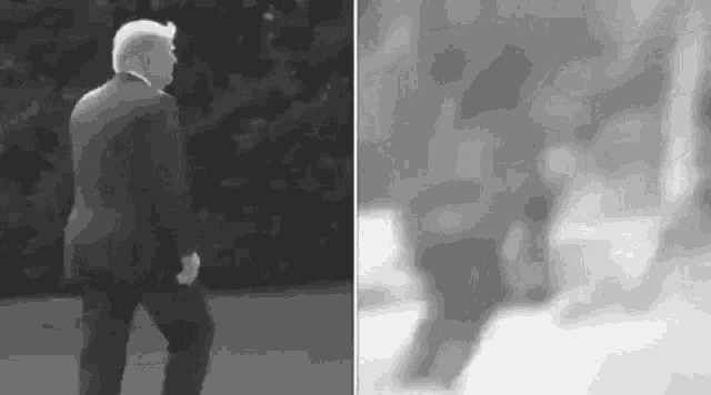 a black and white photo of a man in a suit walking on a sidewalk .