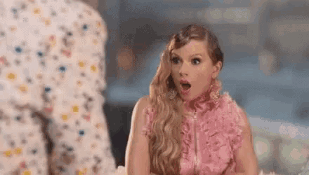 taylor swift is wearing a pink dress and looking surprised .