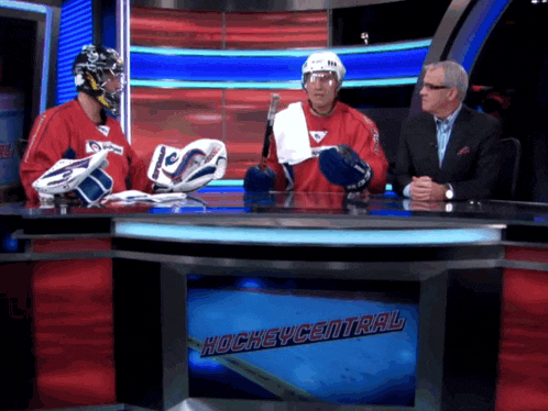 two hockey players are sitting at a table in front of a sign that says hockey central