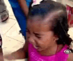 a little girl in a pink dress is crying and making a face .