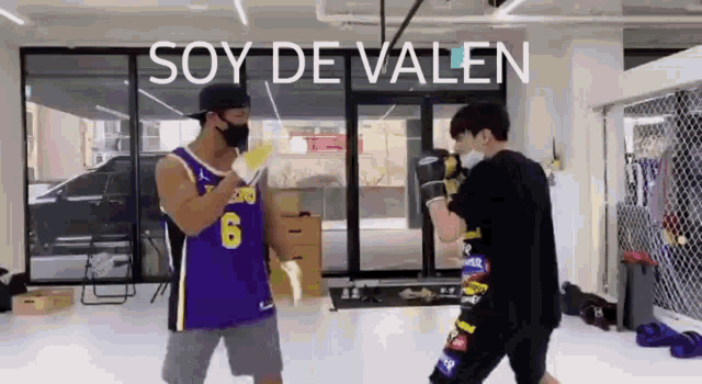 a man in a purple jersey is boxing another man in a gym .