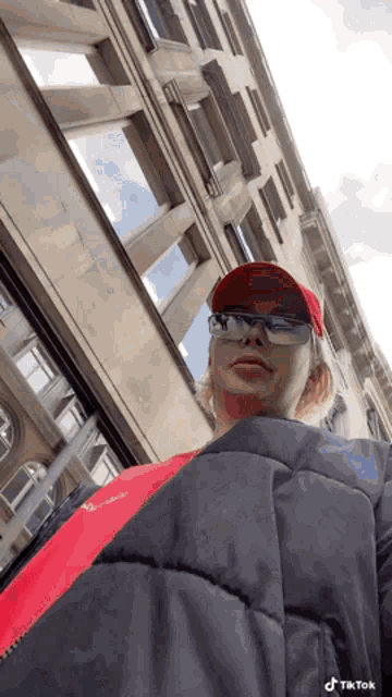 a woman wearing a red hat and glasses is standing in front of a building with tiktok written on the bottom right