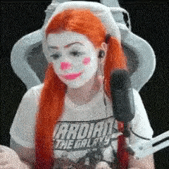 a woman with red hair and white face paint is sitting in front of a microphone wearing a guardians of the galaxy shirt .