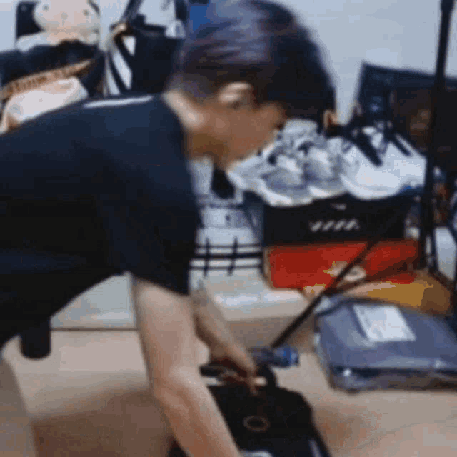 a man in a black shirt is kneeling down in a room with a bunch of shoes on the floor .