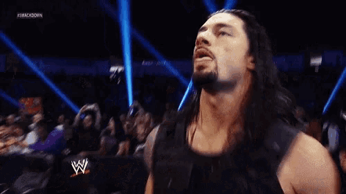 a man with long hair is sticking his tongue out in a wrestling match .