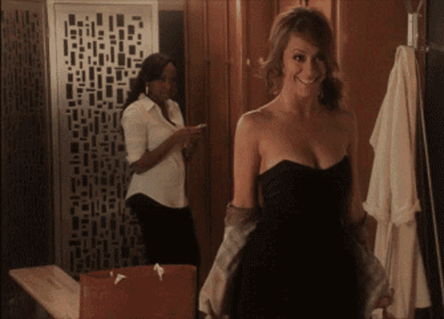a woman in a black strapless dress smiles while another woman looks on