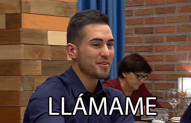 a man is sitting at a table with the word llamame on his shirt