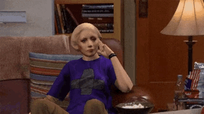 a woman in a purple shirt is sitting on a couch with a bowl of popcorn in front of her