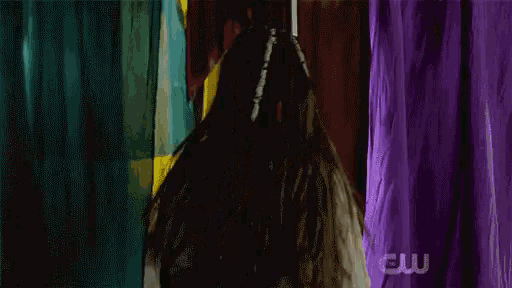a woman with dreadlocks is holding a sword in front of a curtain with the letters cw on it .