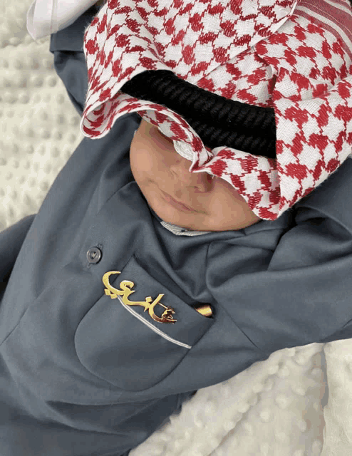 a baby wearing a keffiyeh and a brooch that says ' s ' on it