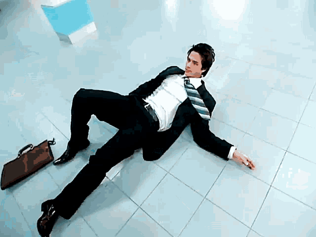 a man in a suit and tie is laying on the floor with a briefcase next to him