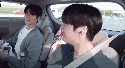 two young men are sitting in the back seat of a car . one of the men is wearing a seat belt .