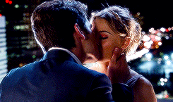 a man in a suit and a woman in a dress are kissing in front of a city skyline .