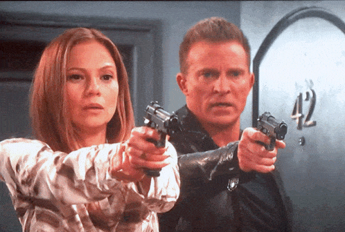 a man and a woman are holding guns in front of a door that has the number 42 on it
