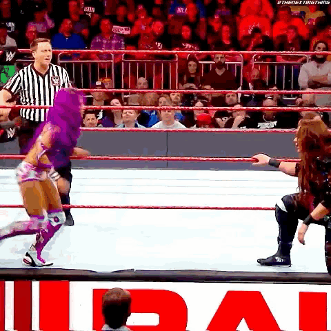 a woman in a purple outfit is standing in a wrestling ring while a referee watches
