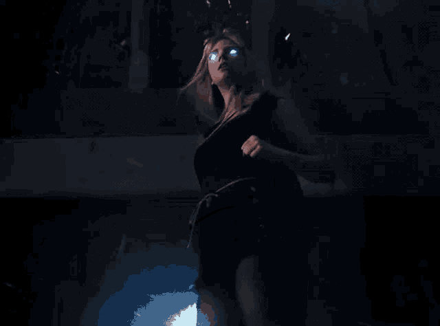 a woman with glowing blue eyes is standing in the dark .