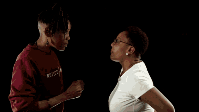 a woman wearing a maroon sweater with the word notice on it talks to another woman wearing a white shirt