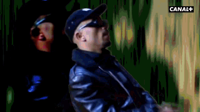 a man in a baseball cap stands in front of two other men and says stop