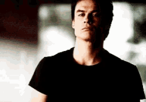 a man in a black shirt is standing in a dark room looking at the camera .