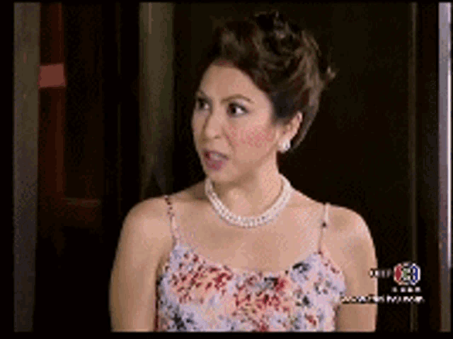 a woman wearing a floral dress and a pearl necklace is on a television screen