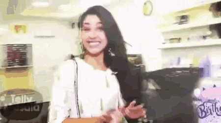 a woman in a white shirt is standing in a room with a birthday cake in the background .