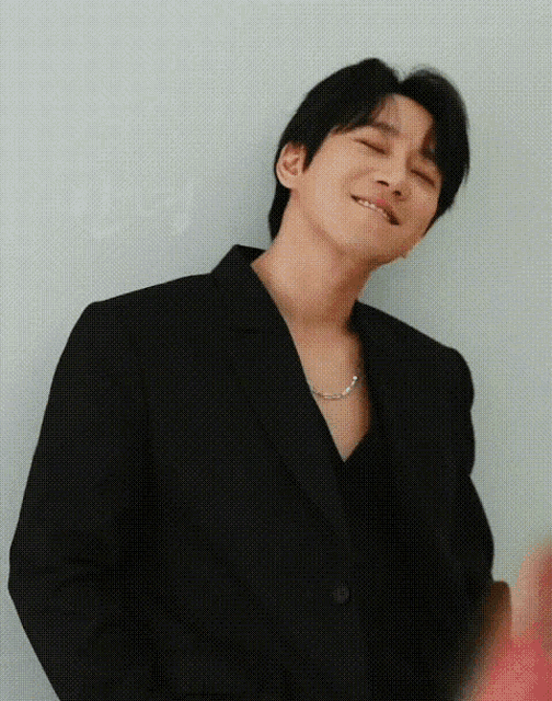 a man wearing a black jacket and a necklace is smiling .