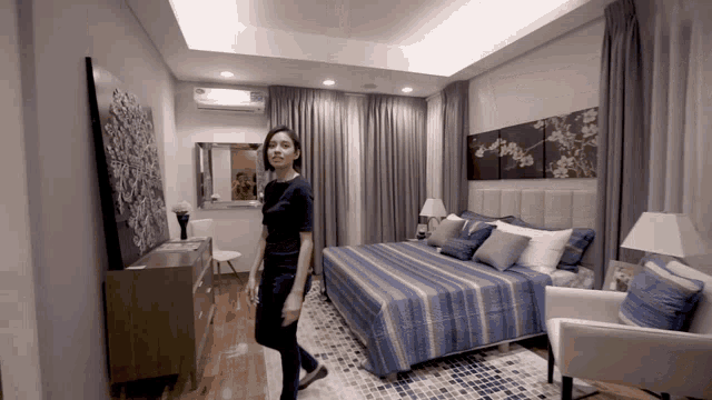 a woman stands in a bedroom with a large bed and a dresser