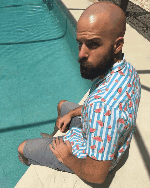 a man in a watermelon shirt sits on the edge of a swimming pool