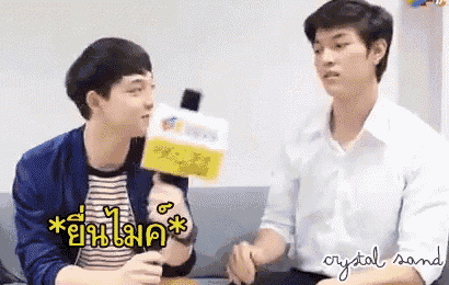two young men are sitting on a couch talking to each other while one of them holds a microphone .