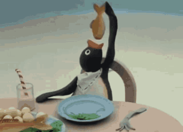 a penguin is sitting at a table with a plate of food on it