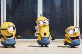 three minions are dancing in front of a window and one is holding a cell phone .