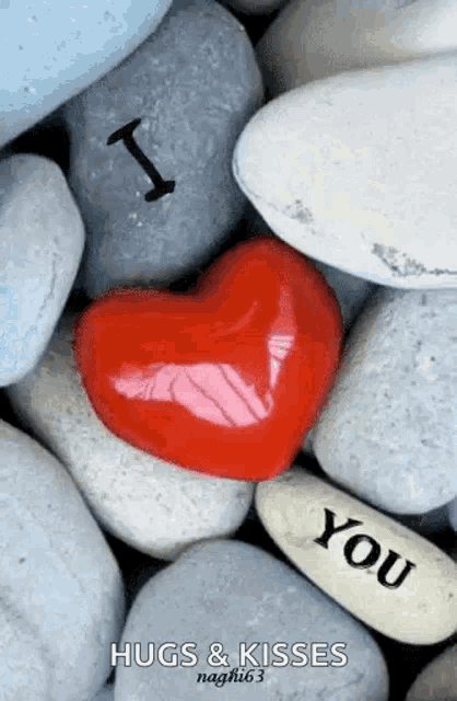 a red heart is sitting on top of a pile of rocks with the words `` i love you '' written on it .