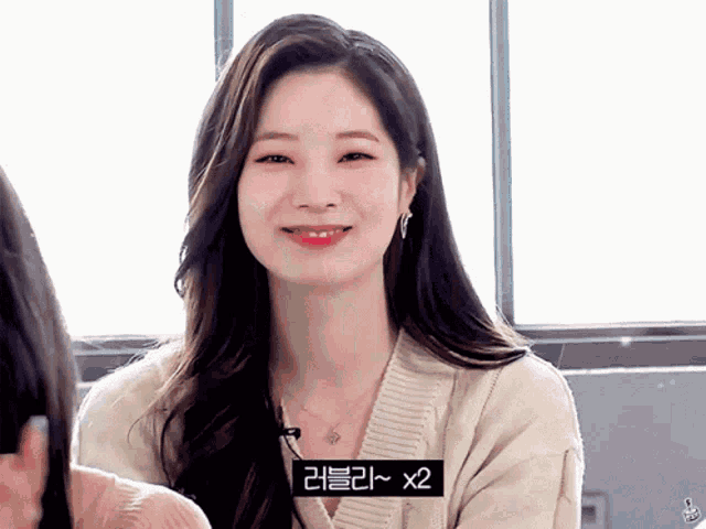 a woman wearing a sweater and a necklace is smiling with a sign that says x2 in the corner