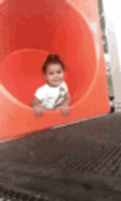 a little girl is sitting on top of an orange slide .