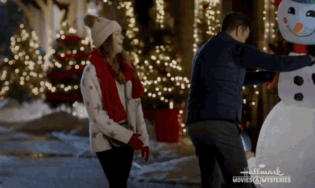 a man and a woman are standing next to a large snowman from hallmark movies and mysteries