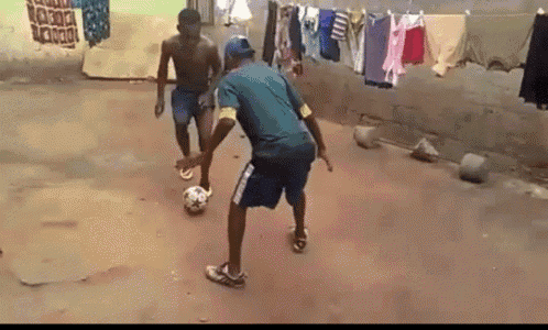 two men are playing soccer in a yard with clothes hanging on a line behind them