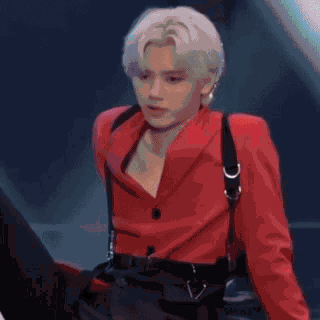 a young man with white hair is wearing a red jacket and black suspenders .