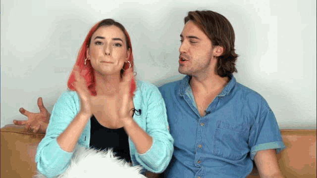 a man and a woman are sitting next to each other on a couch and the woman has pink hair
