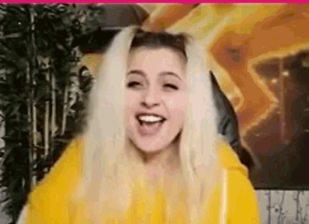 a blonde woman wearing a yellow hoodie is laughing .