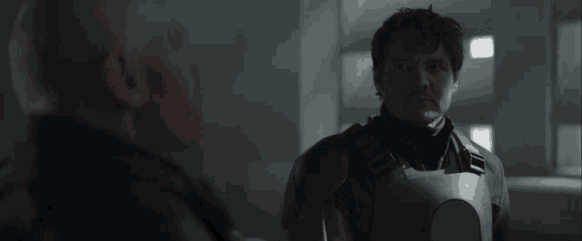 two men are standing next to each other in a dark room and one of them has a mustache .