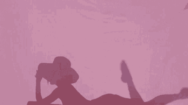 the shadow of a woman laying on her stomach on a pink surface .