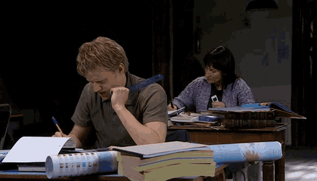 a man and a woman are sitting at a desk with books