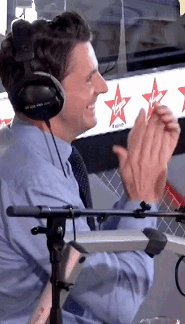 a man wearing headphones applauds in front of a sign that says virgin radio