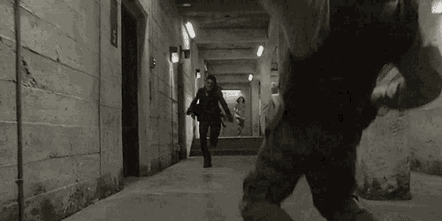 a black and white photo of a man and a woman running down a hallway .