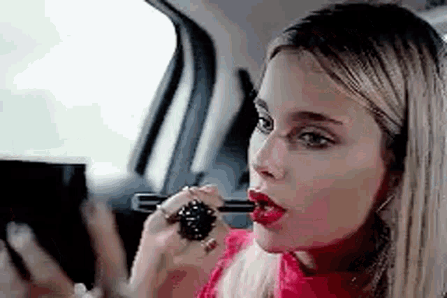 a woman is applying lipstick in a car .