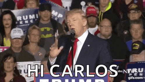 donald trump is speaking into a microphone in front of a crowd of people and says hi carlos