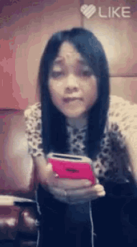 a girl is holding a pink cell phone and a like button is visible in the corner