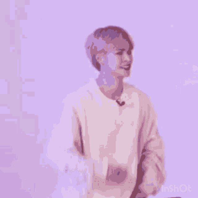 a man in a white sweater is standing in front of a purple wall and dancing .