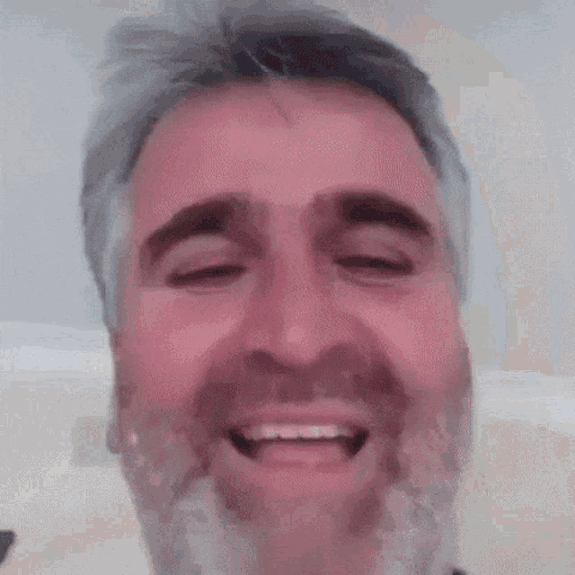 a man with a beard and gray hair is smiling with his eyes closed .