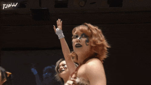 a woman with a tattoo on her face is raising her hand in the air